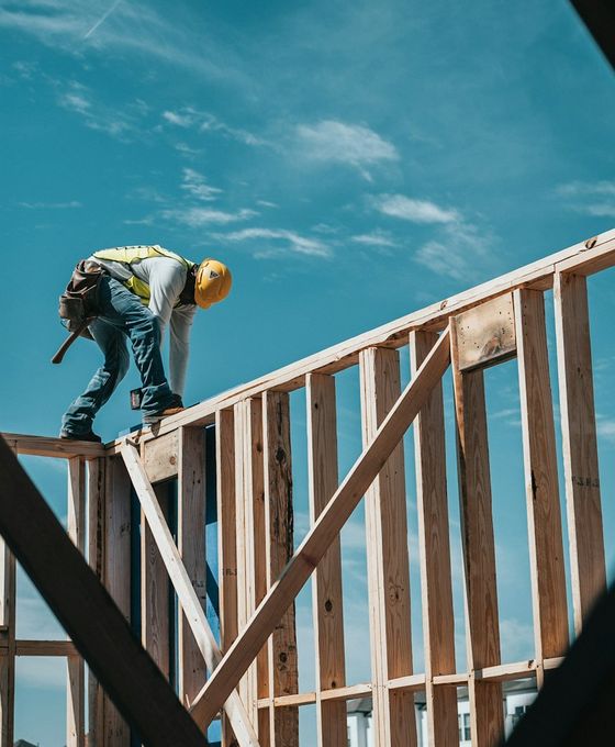Charpentier au travail sur l'ossature bois d'un bâtiment, sous un ciel bleu